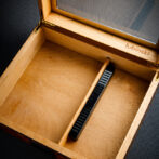 Open wooden box with a black handheld measuring tool resting diagonally inside; inner edge is stamped with 'lubinski'