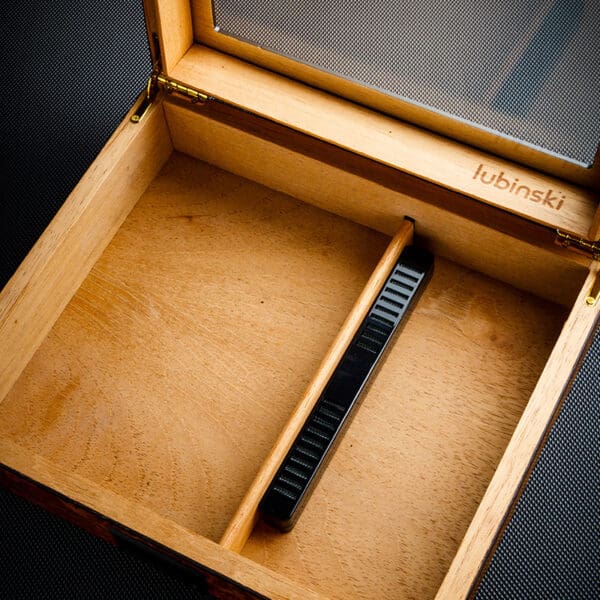 Open wooden box with a black handheld measuring tool resting diagonally inside; inner edge is stamped with 'lubinski'
