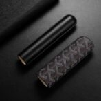 Two cylindrical cosmetic cases, one plain black and one brown patterned, on a dark surface.