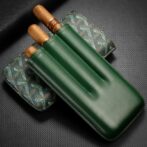 Green leather cigar holder with two cigars partially visible beside a patterned case on a dark background.