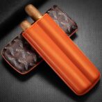 Orange leather double cigar sleeve with two cigars protruding, resting on a brown monogrammed case.