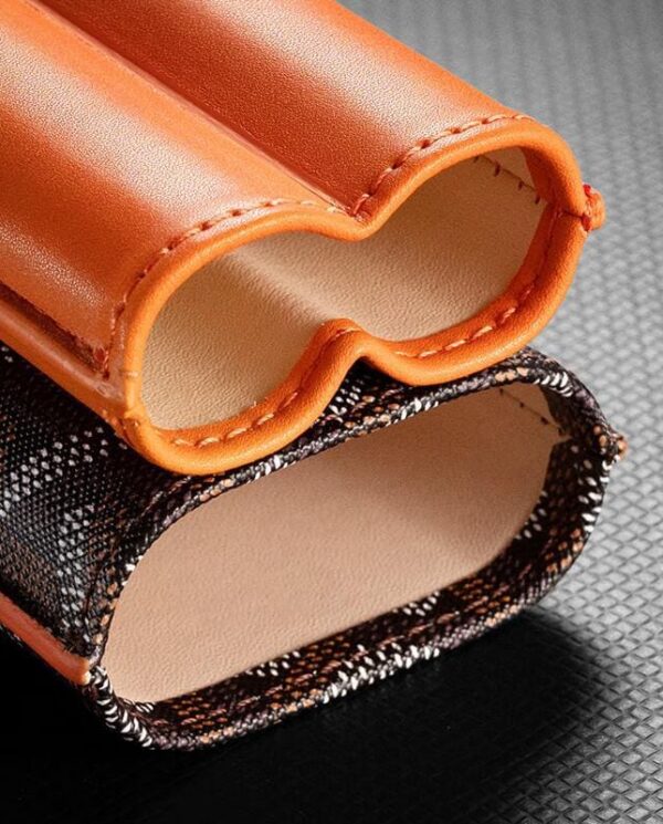 CL033-03 Close-up of two orange leather sleeves with stitched edges, resting on a textured black surface. A patterned fabric panel is visible beneath the sleeves.