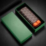 Brown patterned leather wallet inside an open green gift box on a dark surface, gift-ready look.