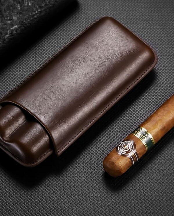 Brown leather cigar case beside a partially smoked cigar on a dark textured surface; a premium smoking accessory set up for display.