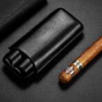 Premium cigar with band lying next to a black leather cigar case on a dark textured surface.