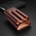 Brown leather card holder with three curved pockets on a dark surface, showing a slim wallet design.