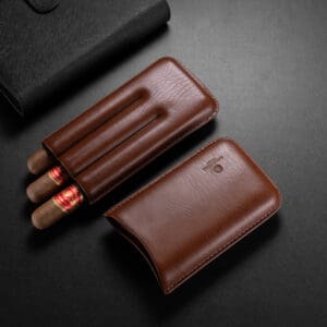 Brown leather cigar case open with three cigars beside a black leather wallet on a dark surface.