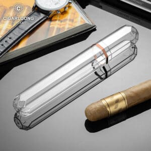 Luxurious smoking accessories on a glossy surface: a clear crystal cigar tube, a brown cigar, a wristwatch, and a CigarLong magazine in the background.