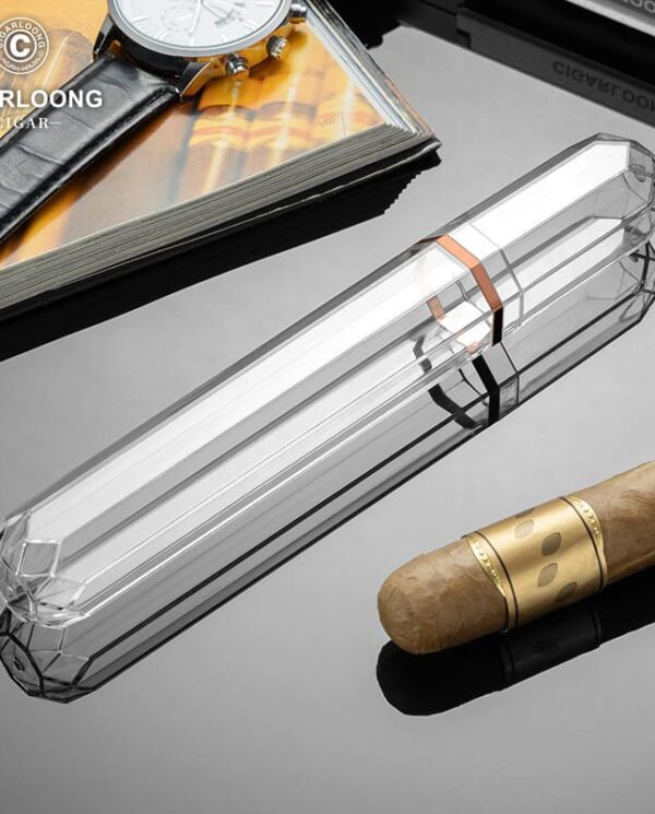 CL037-01 Luxurious smoking accessories on a glossy surface: a clear crystal cigar tube, a brown cigar, a wristwatch, and a CigarLong magazine in the background.