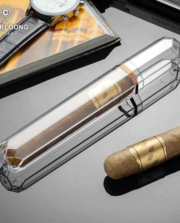 CL037-02 Crystal cigar tube on a reflective surface with a brown cigar nearby and a magazine and watch in the background.