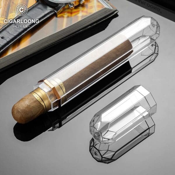 Transparent crystal cigar tube with a brown cigar inside, placed on a reflective black surface; brand logo visible in the corner.