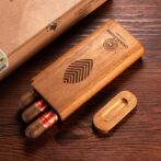 Wooden cigar box with three cigars sticking out on a dark wooden table, lid nearby with carved logo.