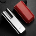Silver vape device with black mouthpiece beside a red leather carry case on a dark textured surface.