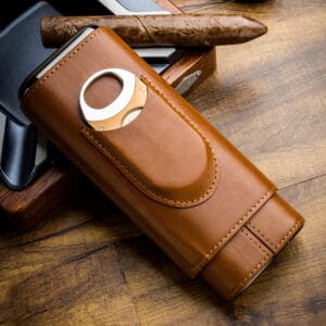 Brown leather cigar case with a built-in circular cutter, resting a cigar on a wooden table.