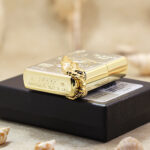 Base stamp and wraparound gold-tone wing on the two-tone Zippo resting on its box