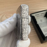 Non-hinge side of the silver-tone lighter with continuous engraved scrollwork
