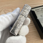 Close-up of the engraved narrow side and lid seam on the silver-tone arabesque Zippo