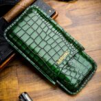 Green crocodile-embossed leather wallet with a gold Urbansky logo on a wooden table surface.