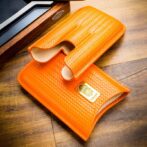 Orange woven leather wallet and matching sleeve on a wooden surface.