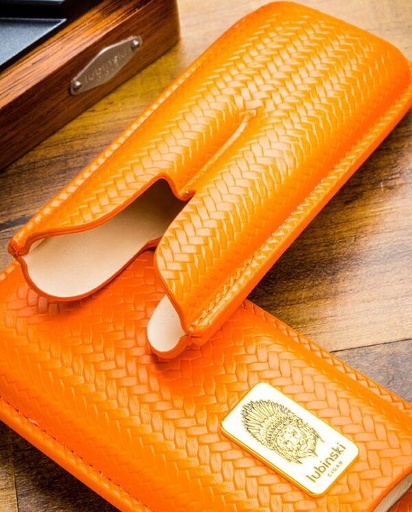 Orange woven leather glasses case, open to reveal beige interior on a wooden table, with a brand plaque visible in the corner.