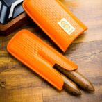 Pair of orange woven leather knife sheaths on a wooden table, with visible blades partially exposed and a label on one sheath.