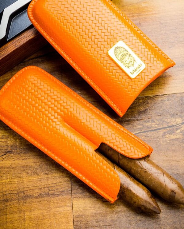 Pair of orange woven leather knife sheaths on a wooden table, with visible blades partially exposed and a label on one sheath.