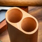 Two adjacent hollow cylindrical holes carved in light wood, forming a twin-hole block seen from an angled top view.