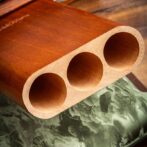 Close-up of a wooden block with three large cylindrical holes, resting on a patterned fabric surface.