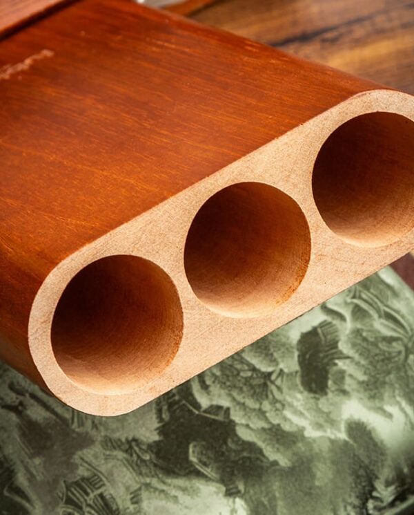 YJA-50030-02 Close-up of a wooden block with three large cylindrical holes, resting on a patterned fabric surface.