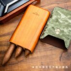 Wooden cigar holder with three cigars protruding, beside a green textured wallet on a wooden desk; disclaimer in Chinese notes props for display.