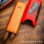 Wooden cigar tube with two cigars emerging, placed beside a red case featuring a black horse illustration on a wooden surface.