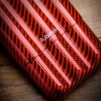 Close-up of a red carbon-fiber patterned phone case with white diagonal stripes on a wooden surface.