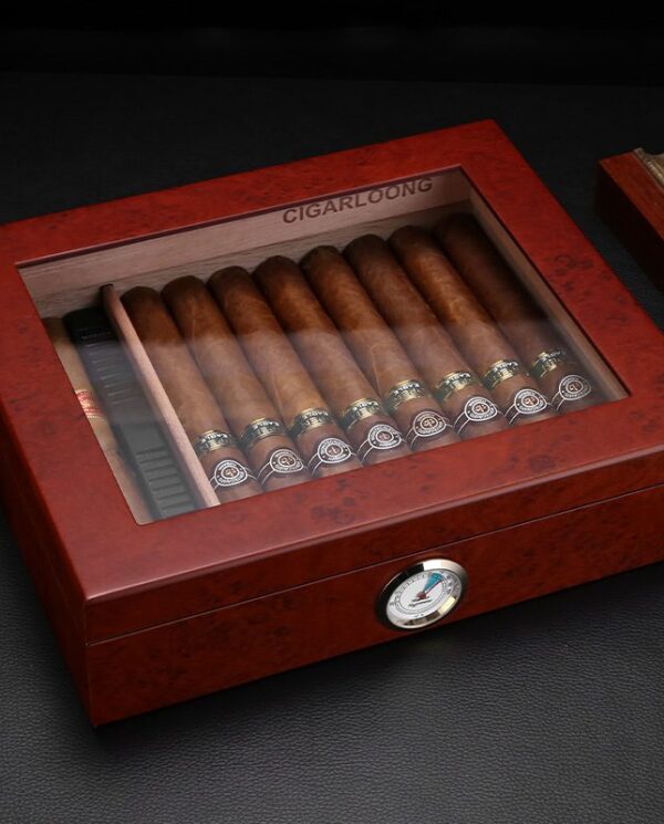Wooden cigar humidor with glass top displaying a row of cigars and a hygrometer on the front.
