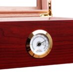 Close-up of a brass-framed hygrometer embedded in dark wood, indicating humidity levels on a humidor surface.