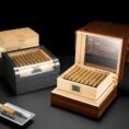 Luxury wooden cigar humidor with glass lid, open to reveal neatly packed cigars and a digital humidity gauge reading around 70%.
