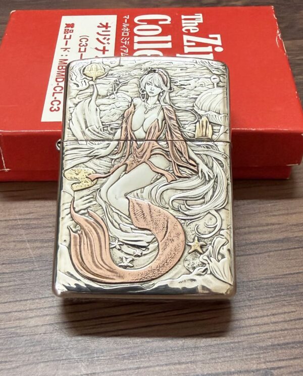 KZ003 Ornate metal tin with a mermaid illustration resting against a red box on a wooden table.