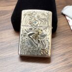 Brass Zippo lighter with an engraved mermaid among waves and sea creatures, a blue gem at her chest.
