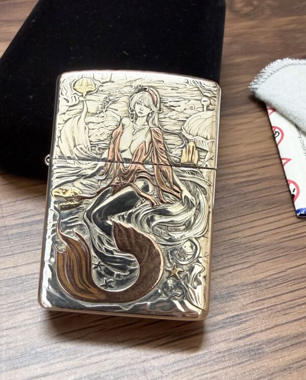 KZ003_03 Silver engraved lighter showing a mermaid with flowing hair amid waves and rocks in a coastal scene.