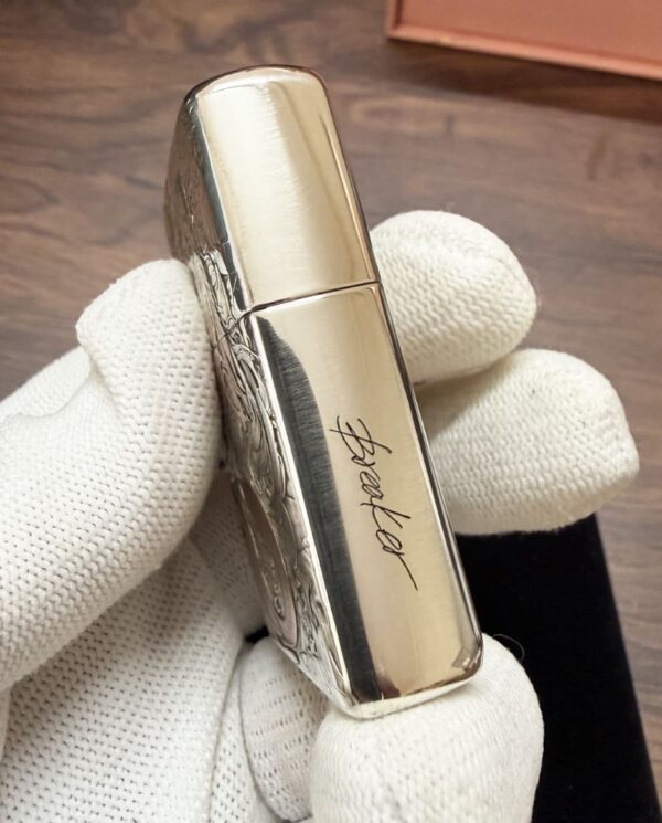 KZ003_04 Shiny silver lipstick case with decorative engraving, held by a white-gloved hand. The side shows a cursive signature.