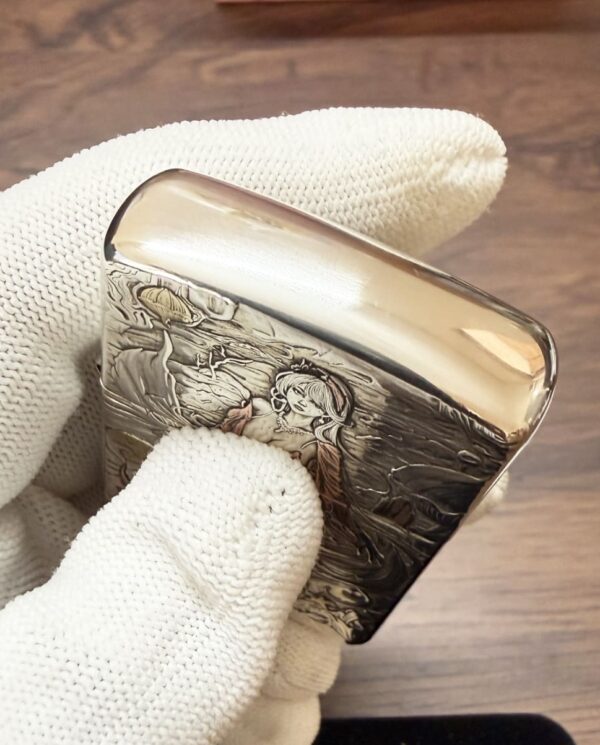 KZ003_12 Close-up of a decorative metal cigarette case with an engraved scene of a woman in a landscape, held by gloved hands