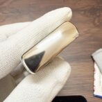 Polished gold-toned rectangular cigarette case held by gloved hand against a wooden background.