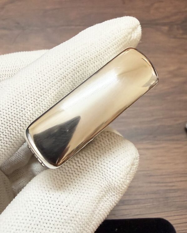 KZ003_13 Polished gold-toned rectangular cigarette case held by gloved hand against a wooden background.