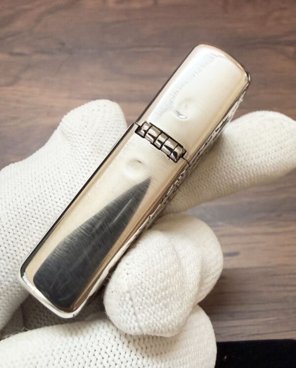 KZ003_15 Close-up of a polished silver lighter being held by a white glove-drapped hand.