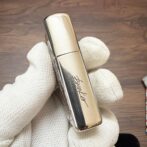 Close-up of a gold, reflective lipstick tube held by a gloved hand.