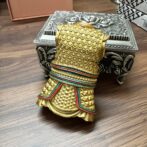Decorative gold-toned fist sculpture with layered bracelets leaning on an ornate silver box on a wooden table.