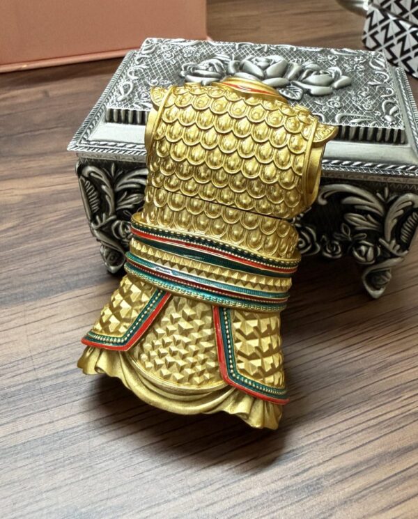 Decorative gold-toned fist sculpture with layered bracelets leaning on an ornate silver box on a wooden table.