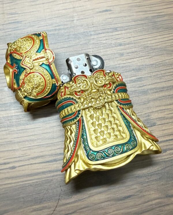 Ornate gold and teal metal lighter shaped like ceremonial armor, open to reveal the flint chamber inside a decorative grip area