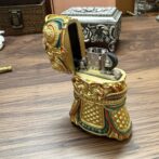 Ornate, gold-toned lighter shaped like a decorative boot with intricate designs and a hinged lid.