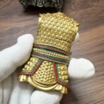 Close-up of a gold, scale-pattern ceremonial cuff with red, green, and teal enamel bands.”,