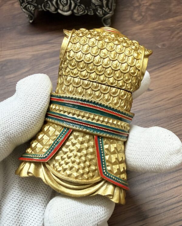 Close-up of a gold, scale-pattern ceremonial cuff with red, green, and teal enamel bands.”,